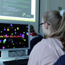 A girl, sitting in front of a computer screen, coding her individual screen saver.