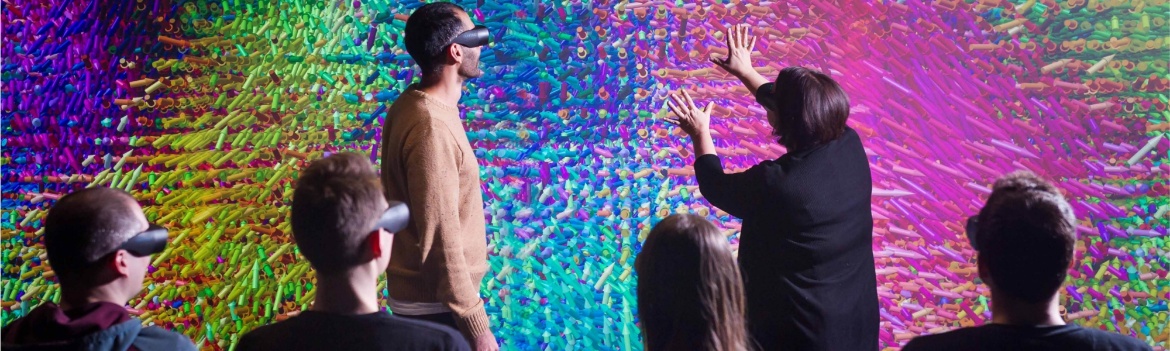 A group of researchers discusses a colorful visualization projected on a powerwall.